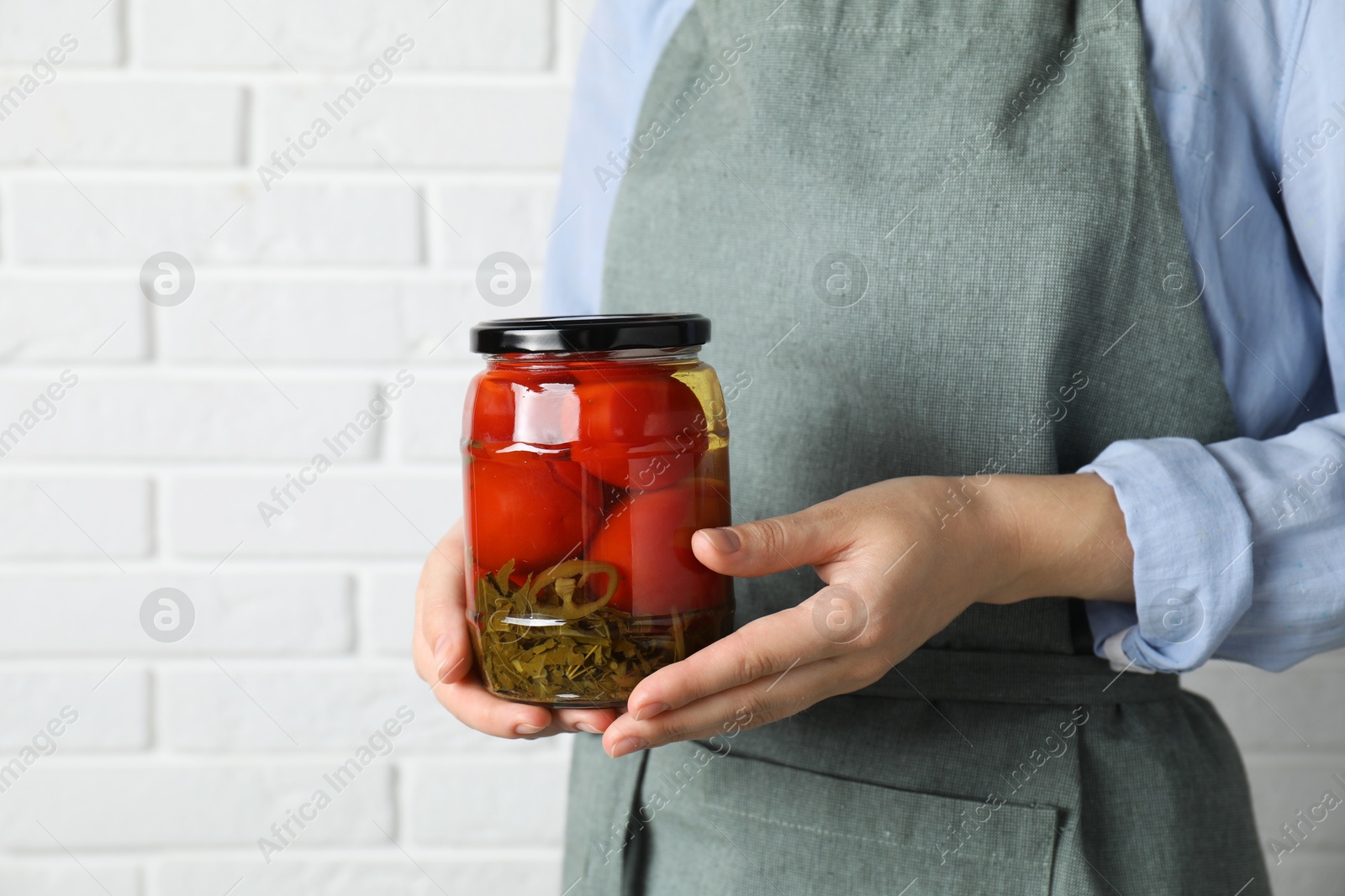 Photo of Woman holding jar with tasty pickled tomatoes against white brick wall, closeup. Space for text