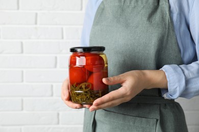 Woman holding jar with tasty pickled tomatoes against white brick wall, closeup. Space for text