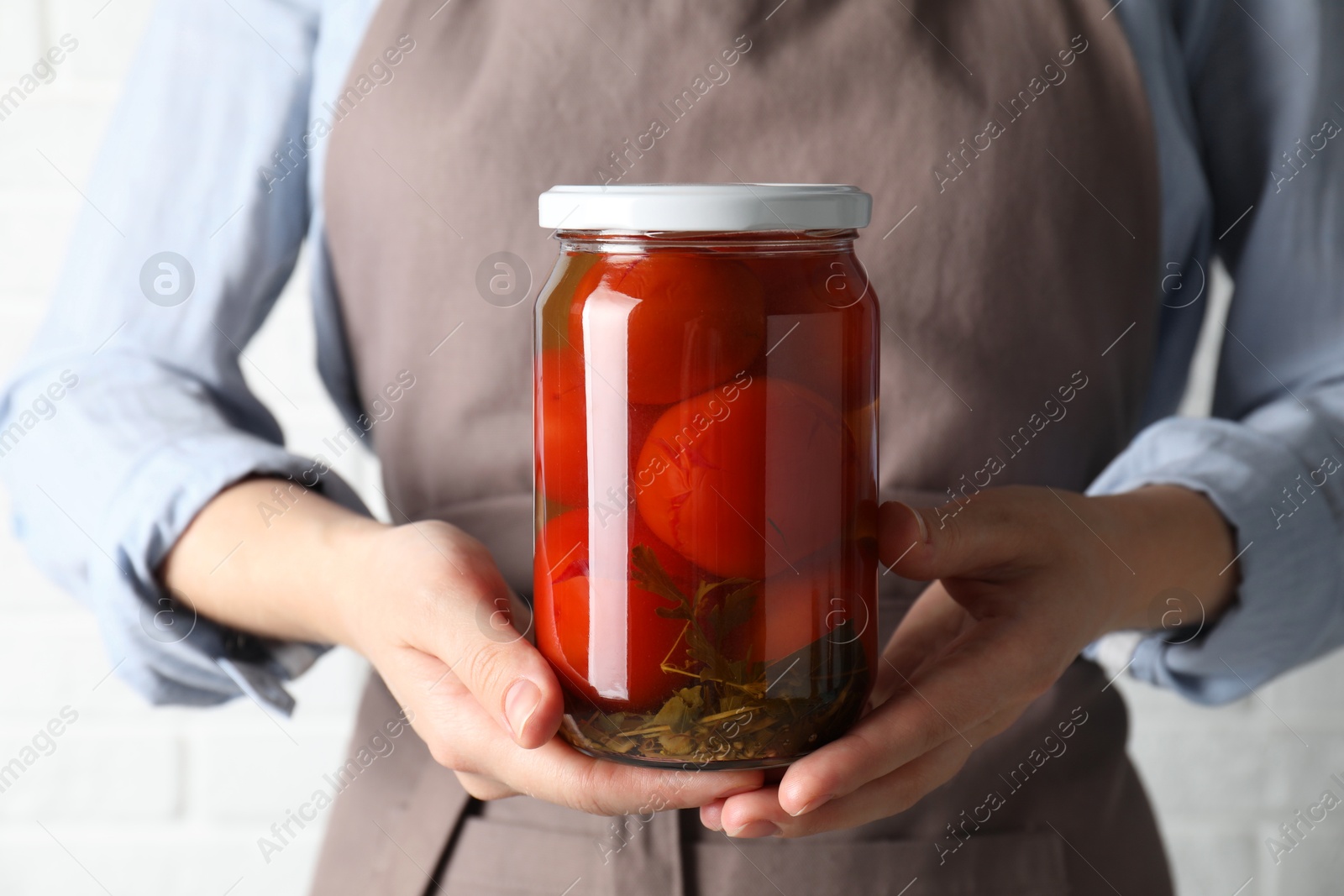 Photo of Woman holding jar with tasty pickled tomatoes on light background, closeup