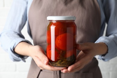 Photo of Woman holding jar with tasty pickled tomatoes on light background, closeup