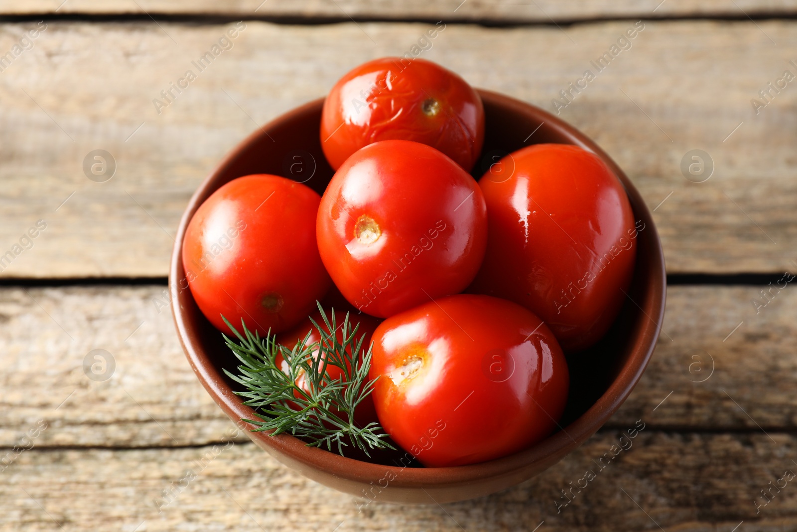 Photo of Tasty pickled tomatoes and dill in bowl on wooden table