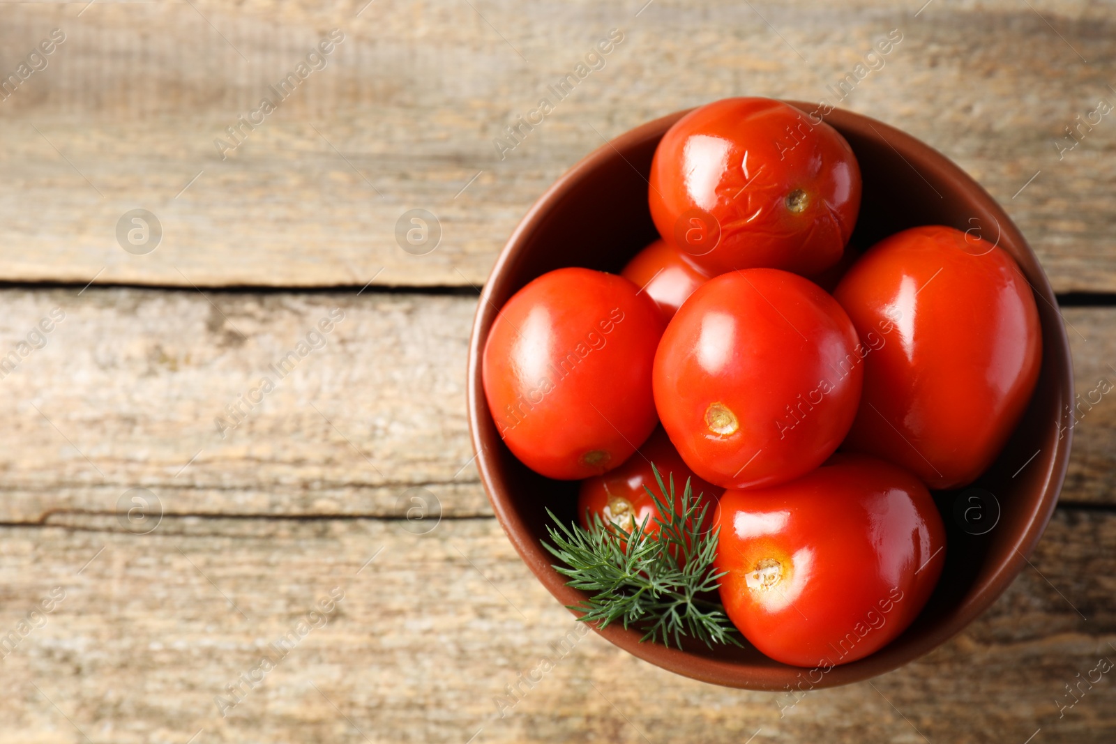 Photo of Tasty pickled tomatoes and dill in bowl on wooden table, top view. Space for text