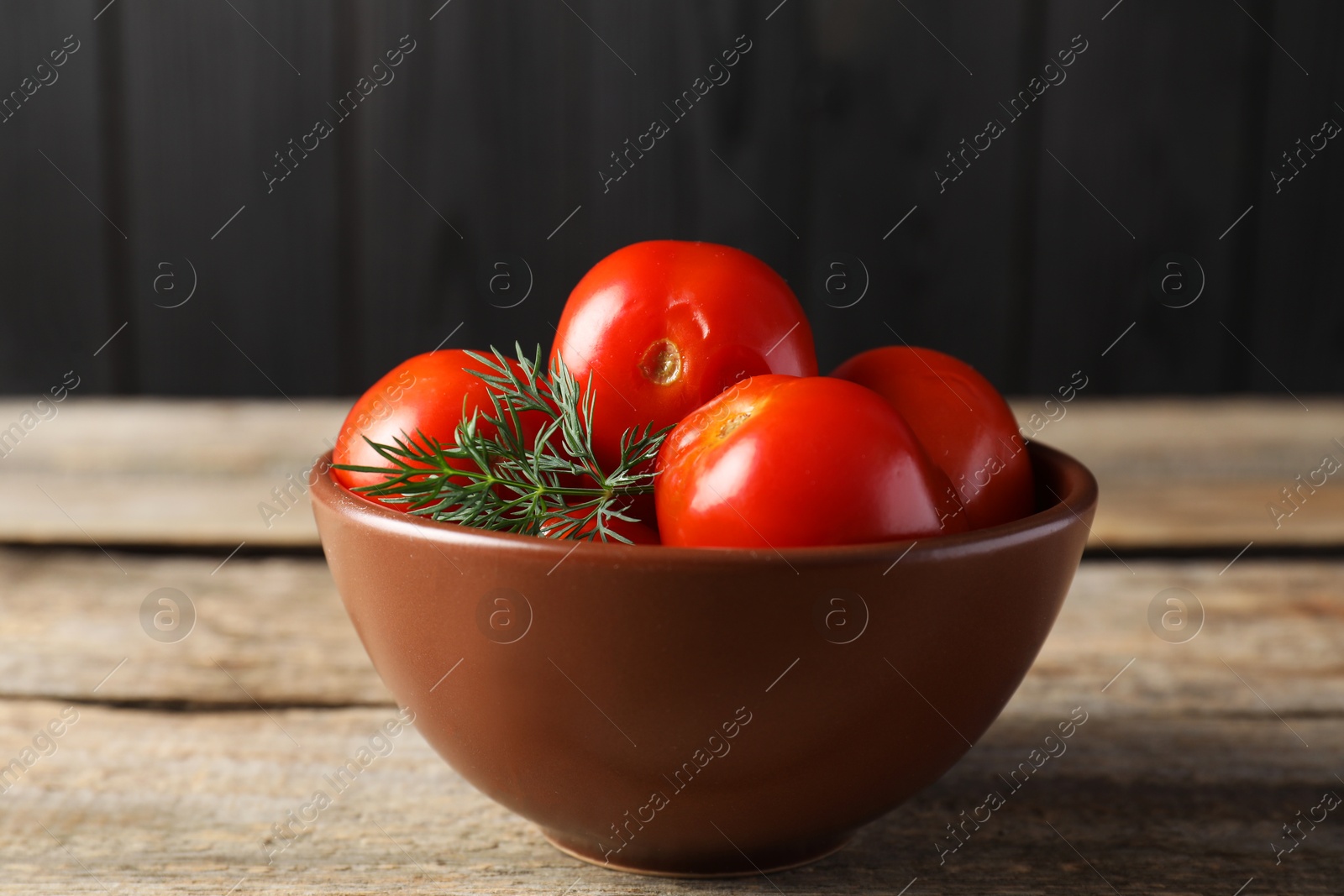 Photo of Tasty pickled tomatoes and dill in bowl on wooden table