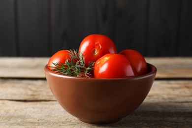 Photo of Tasty pickled tomatoes and dill in bowl on wooden table