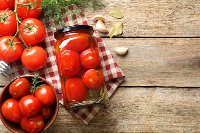 Tasty pickled tomatoes in jar, spices and fresh vegetables on wooden table, top view. Space for text