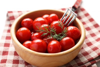 Tasty pickled tomatoes in bowl, dill and fork on table, closeup