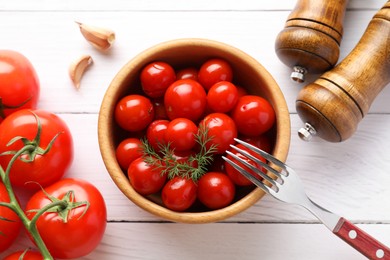 Photo of Tasty pickled tomatoes in bowl, fresh vegetables, dill, garlic and fork on white wooden table, top view