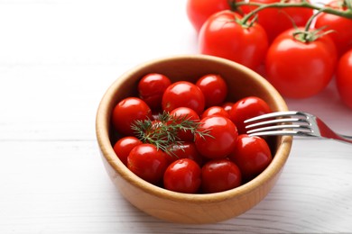 Photo of Tasty pickled tomatoes in bowl, fresh vegetables, dill and fork on white wooden table