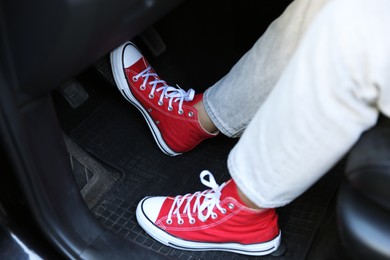 Photo of Woman in sneakers pushing on pedal of car brake, closeup