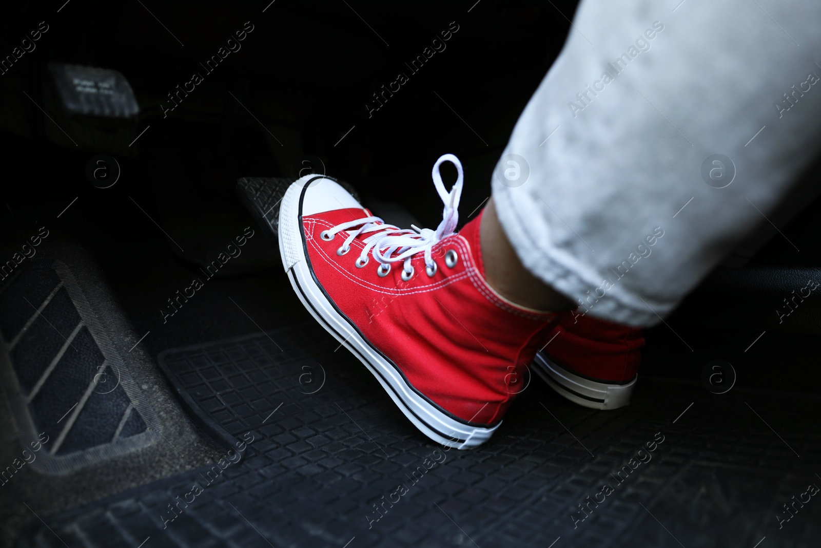 Photo of Woman in sneakers pushing on pedal of car brake, closeup