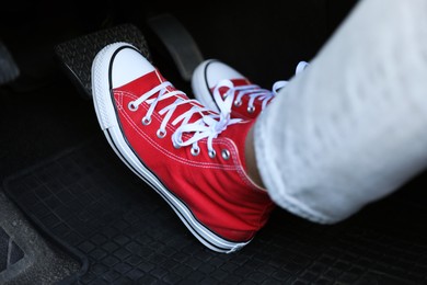 Photo of Woman in sneakers pushing on pedal of car brake, closeup