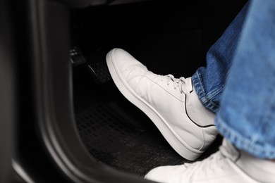 Man in sneakers pushing on pedal of car brake, closeup