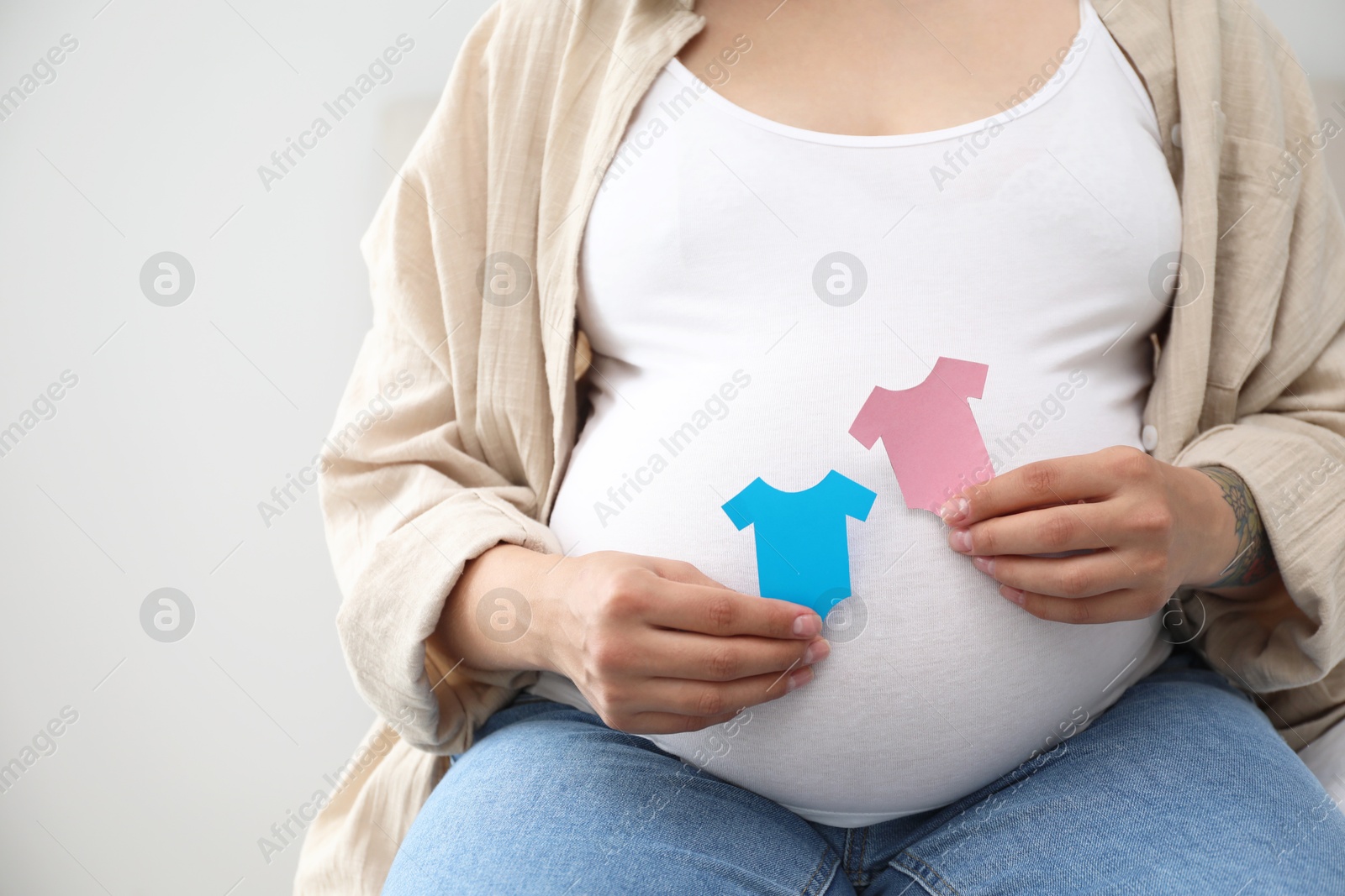 Photo of Pregnant woman with paper T-shirts on light gray background, closeup. Expecting twins