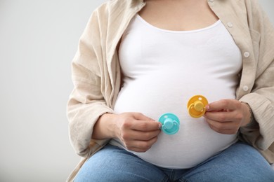 Pregnant woman with pacifiers on light gray background, closeup and space for text. Expecting twins