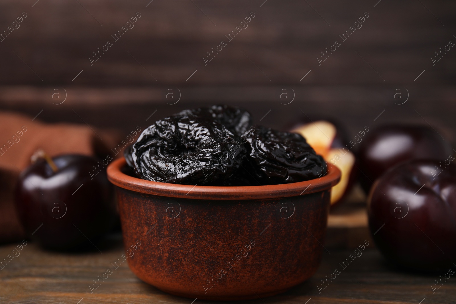 Photo of Tasty dried plums (prunes) in bowl on wooden table, closeup