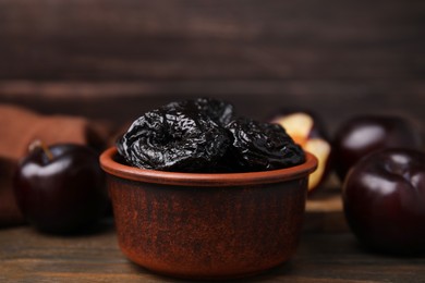 Photo of Tasty dried plums (prunes) in bowl on wooden table, closeup