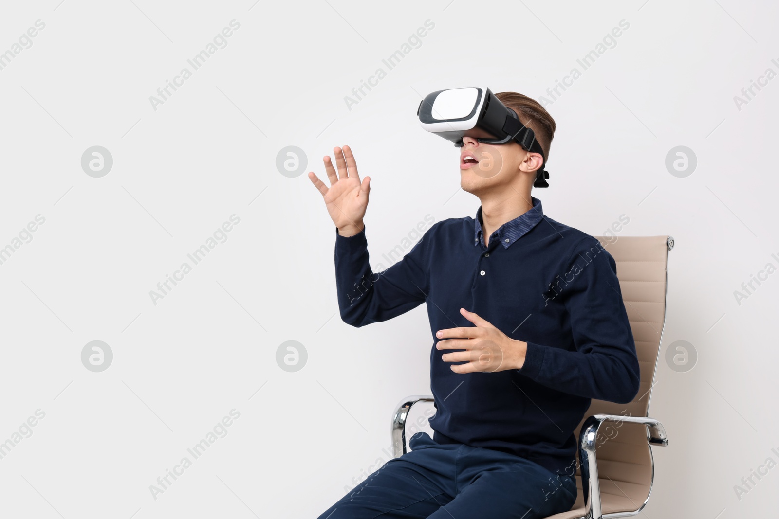 Photo of Emotional young man with virtual reality headset sitting on chair near white wall, space for text