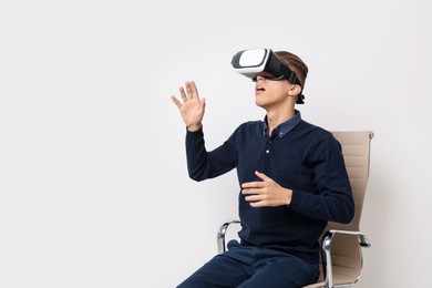 Emotional young man with virtual reality headset sitting on chair near white wall, space for text