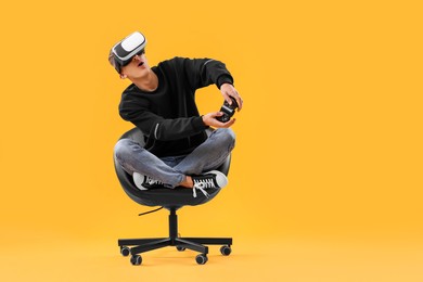 Photo of Emotional young man with virtual reality headset and controller sitting on chair against yellow background