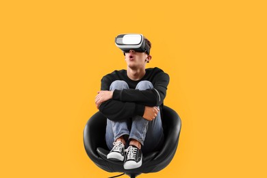 Photo of Emotional young man with virtual reality headset sitting on chair against yellow background
