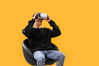 Emotional young man with virtual reality headset sitting on chair against yellow background, space for text