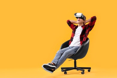 Photo of Happy young man with virtual reality headset sitting on chair against yellow background, space for text