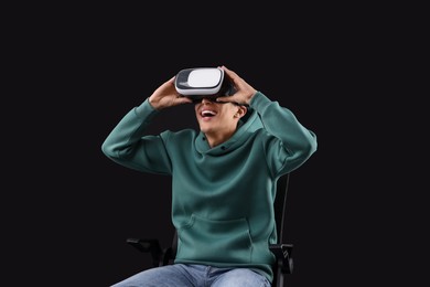 Photo of Happy young man with virtual reality headset sitting on chair against black background