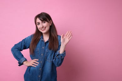 Happy young woman waving on pink background, space for text