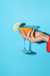 Photo of Woman with glass of refreshing cocktail on light blue background, closeup