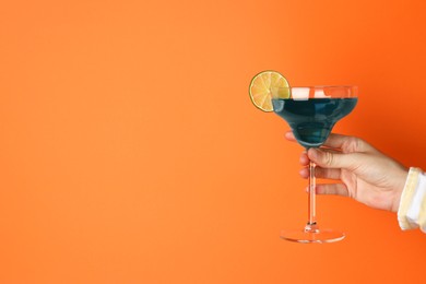 Photo of Woman with glass of refreshing cocktail on orange background, closeup. Space for text