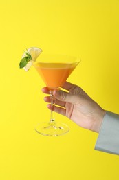 Photo of Woman with glass of refreshing cocktail on yellow background, closeup