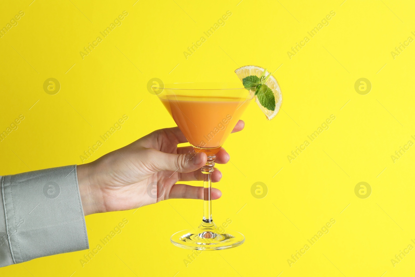 Photo of Woman with glass of refreshing cocktail on yellow background, closeup