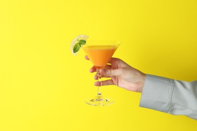 Photo of Woman with glass of refreshing cocktail on yellow background, closeup