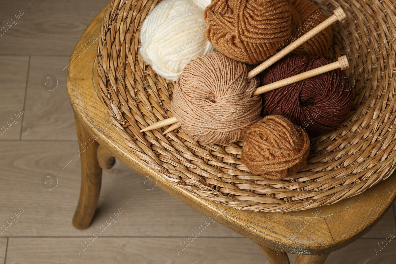 Photo of Skeins of different yarn, knitting needles and wicker mat on chair indoors