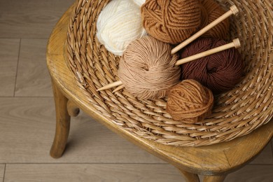 Photo of Skeins of different yarn, knitting needles and wicker mat on chair indoors