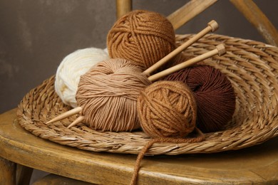 Photo of Skeins of different yarn, knitting needles and wicker mat on chair, closeup