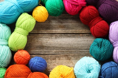 Photo of Frame of different bright yarns on wooden table, flat lay. Space for text