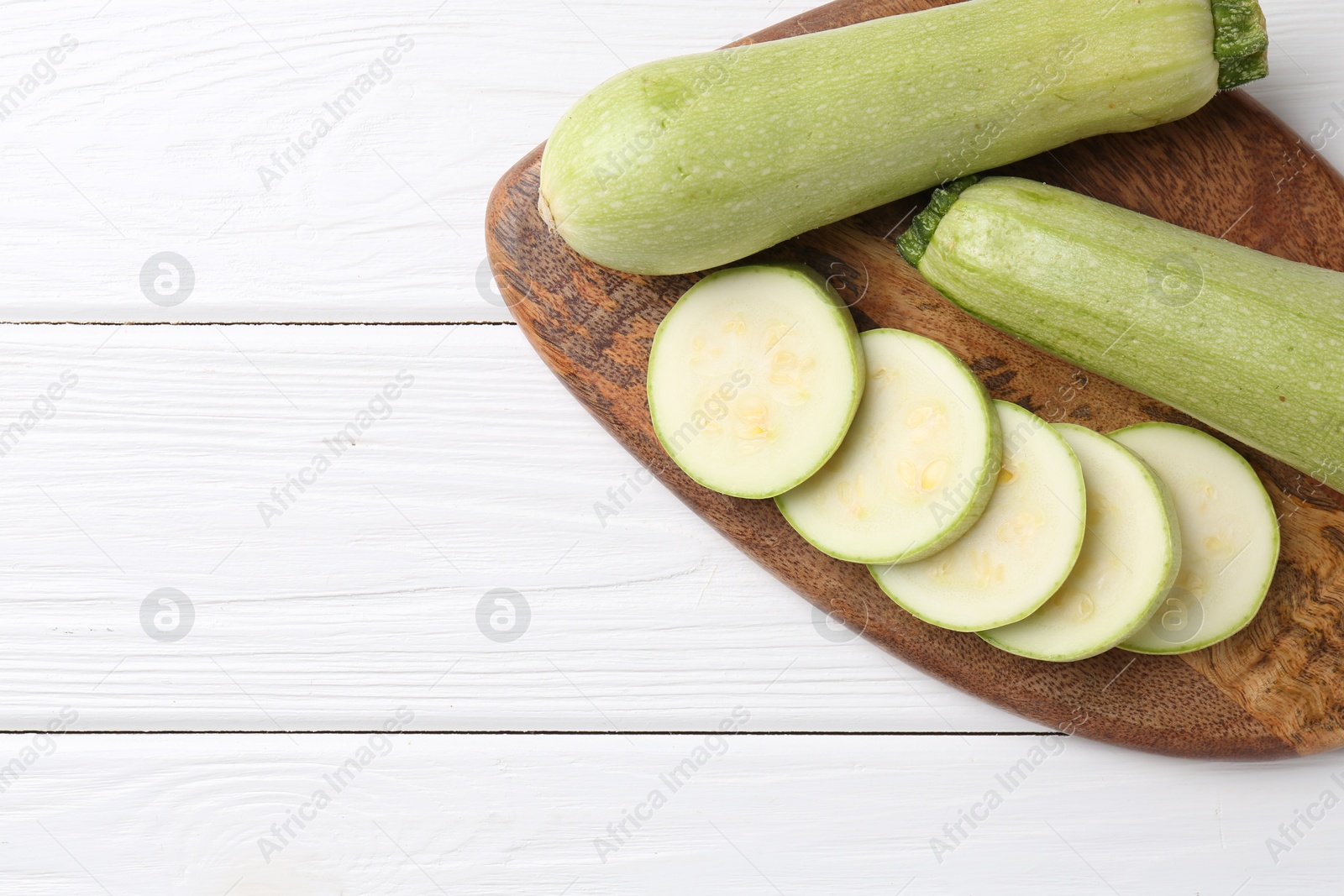 Photo of Board with fresh zucchinis on white wooden table, top view. Space for text