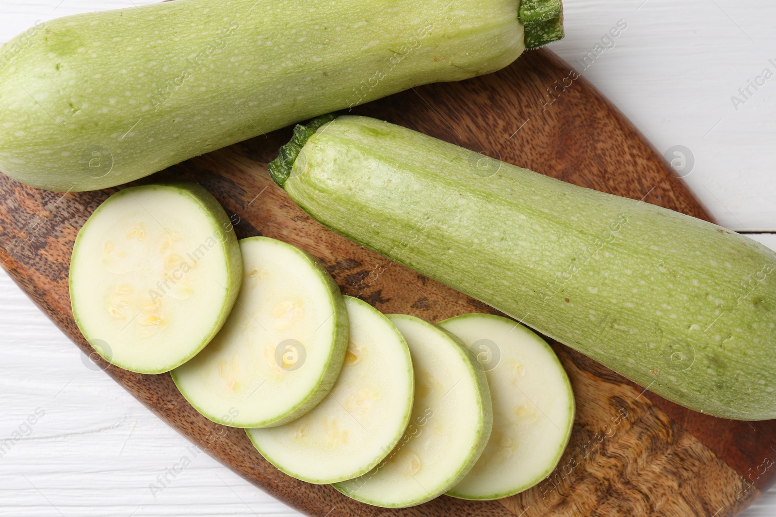 Photo of Board with fresh zucchinis on white wooden table, top view