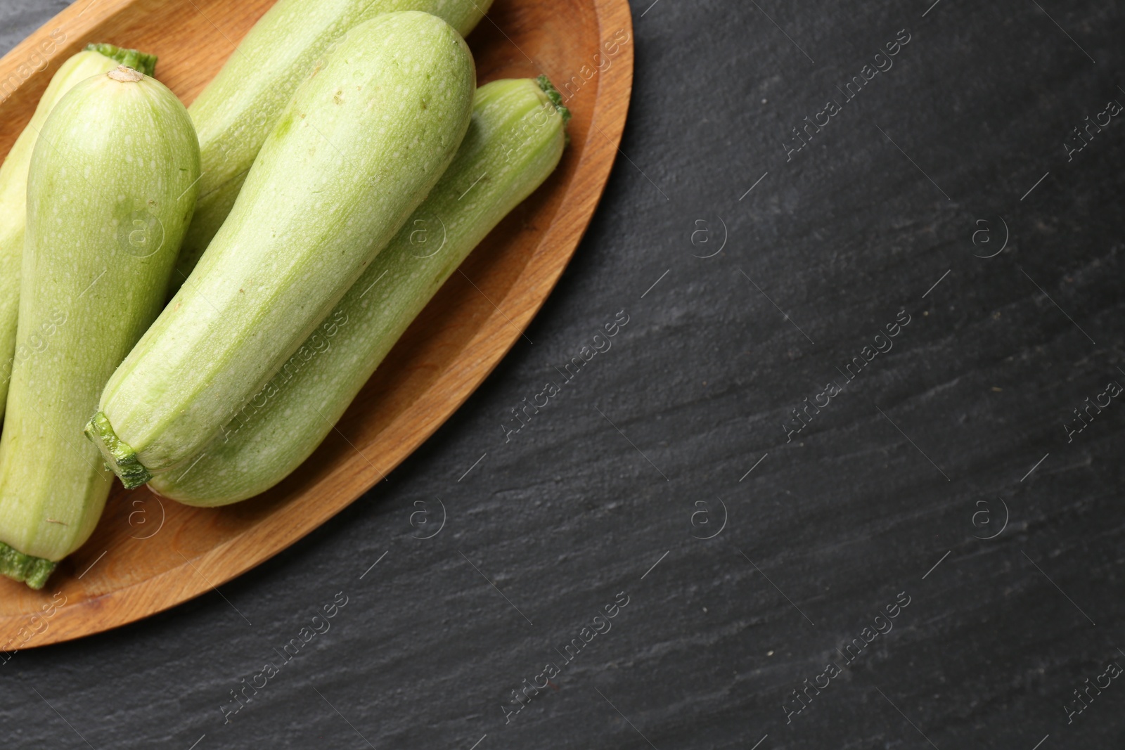 Photo of Fresh zucchinis on dark textured table, top view. Space for text