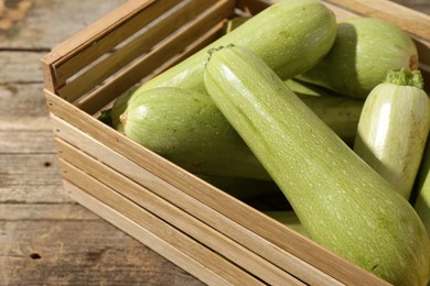 Photo of Crate with fresh zucchinis on wooden table, closeup