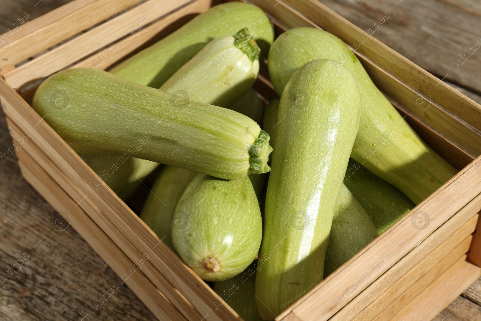 Photo of Crate with fresh zucchinis on wooden table, closeup