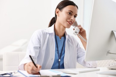 Photo of Smiling nurse consulting patient by phone at table in clinic