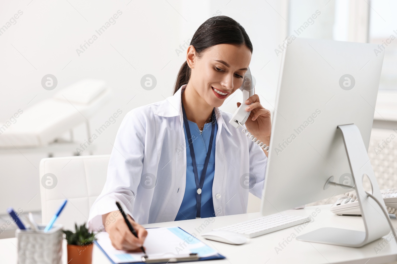 Photo of Smiling nurse consulting patient by phone at table in clinic