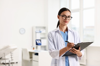 Beautiful nurse with clipboard writing notes in clinic. Space for text