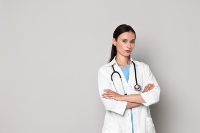 Beautiful nurse with crossed arms on grey background. Space for text