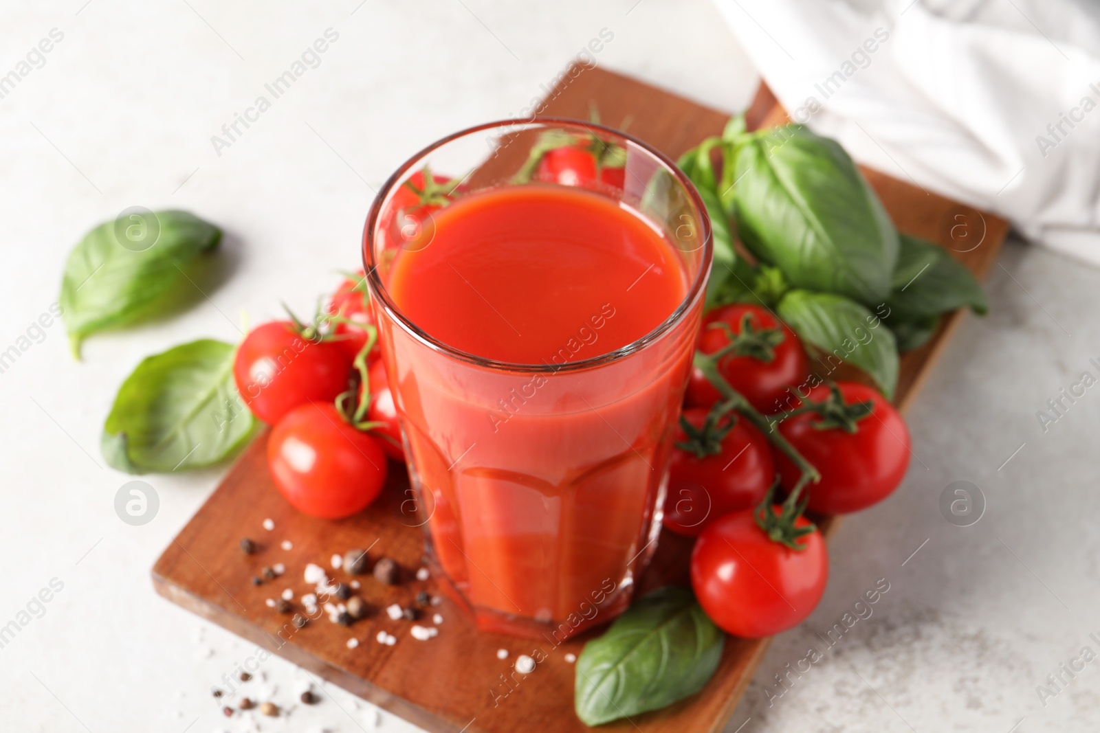 Photo of Tasty tomato juice in glass, spices and fresh vegetables on light table