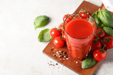 Photo of Tasty tomato juice in glass, spices and fresh vegetables on light table, space for text