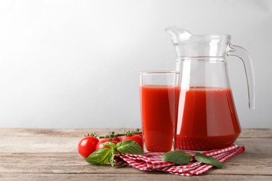 Photo of Tasty tomato juice with basil leaves and fresh vegetables on wooden table, space for text