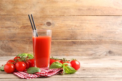 Tasty tomato juice in glass with basil leaves and fresh vegetables on wooden table, space for text